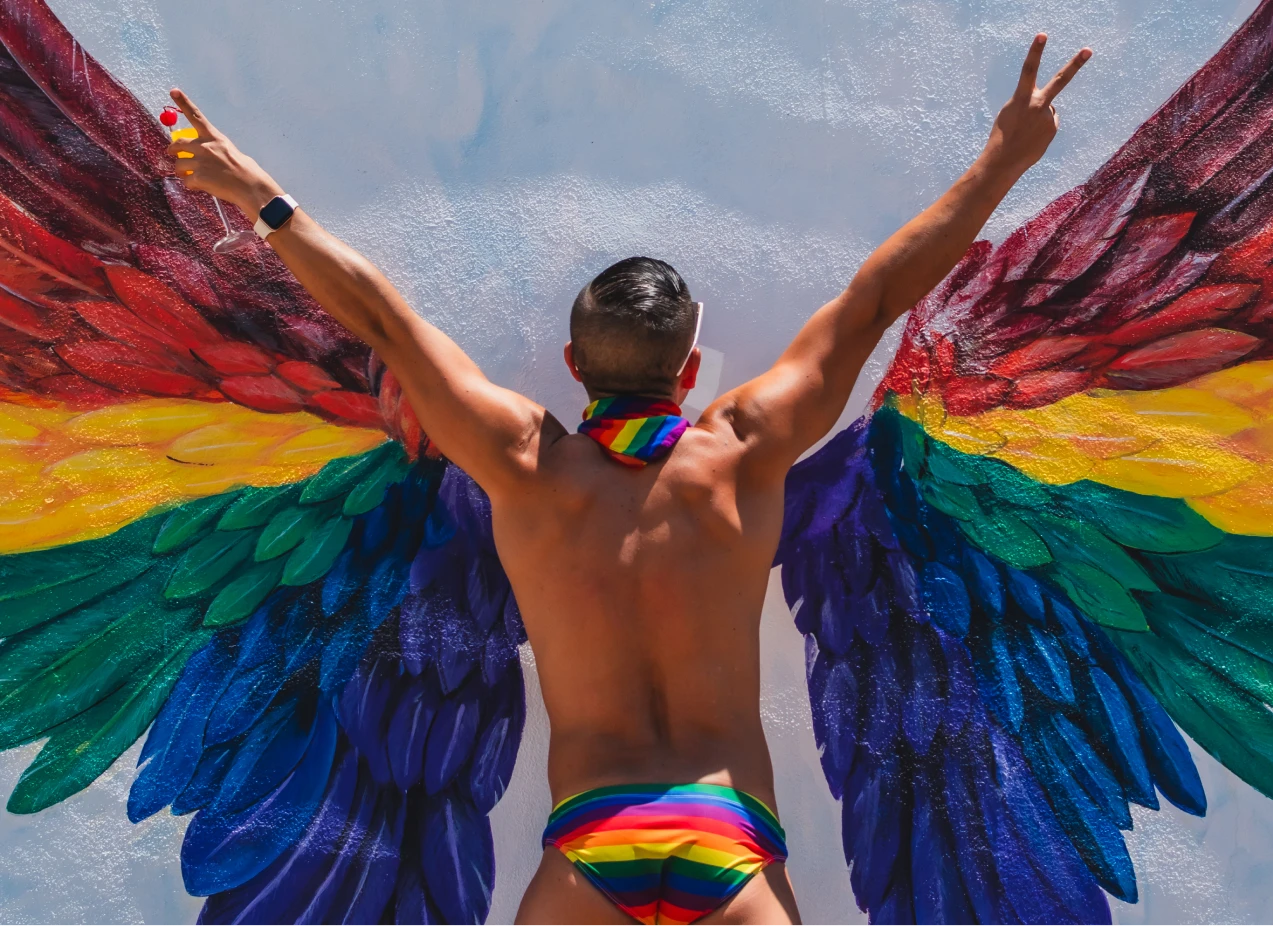 Hombre con alas de colores arco&iacute;ris y manillas, celebrando en el agua