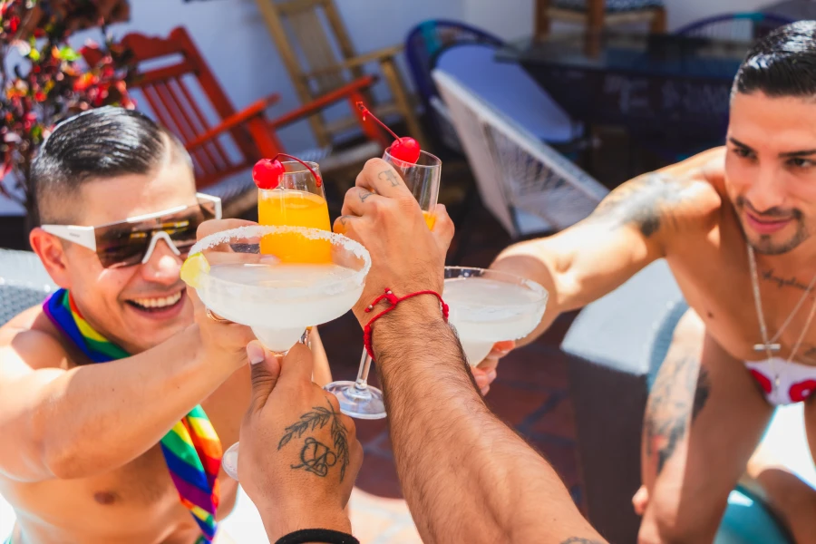 Tres amigos levantan copas con c&oacute;cteles y sombrillas de coraz&oacute;n en la piscina