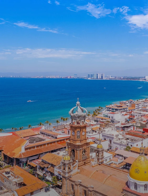 Vista de la costa y mar azul desde un campanario sobre tejados blancos.