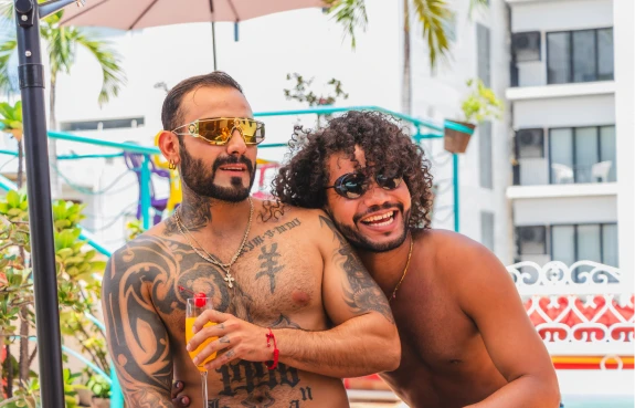 Dos hombres con gafas de sol y cerveza abrazados en un ambiente tropical