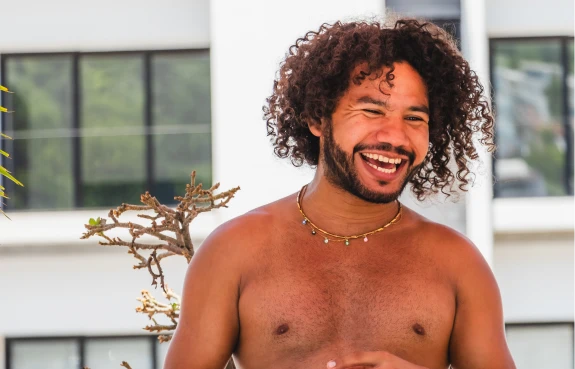 Hombre sonriente con cabello rizado, al aire, frente a un edificio