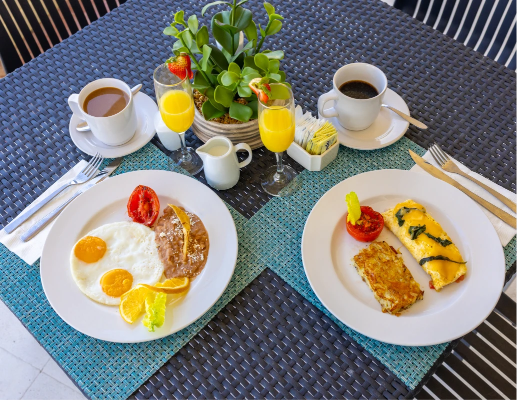 Desayuno en mesa: huevos, omelet y caf&eacute; con jugos y decoraci&oacute;n floral