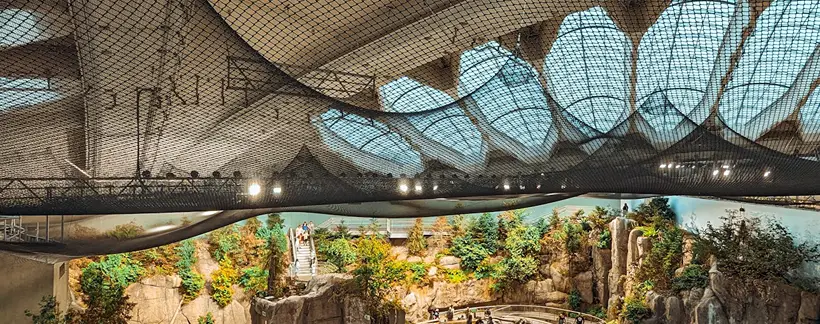 Vista interior de un acuario con arrecifes rocosos, vegetaci&oacute;n y tiburones.