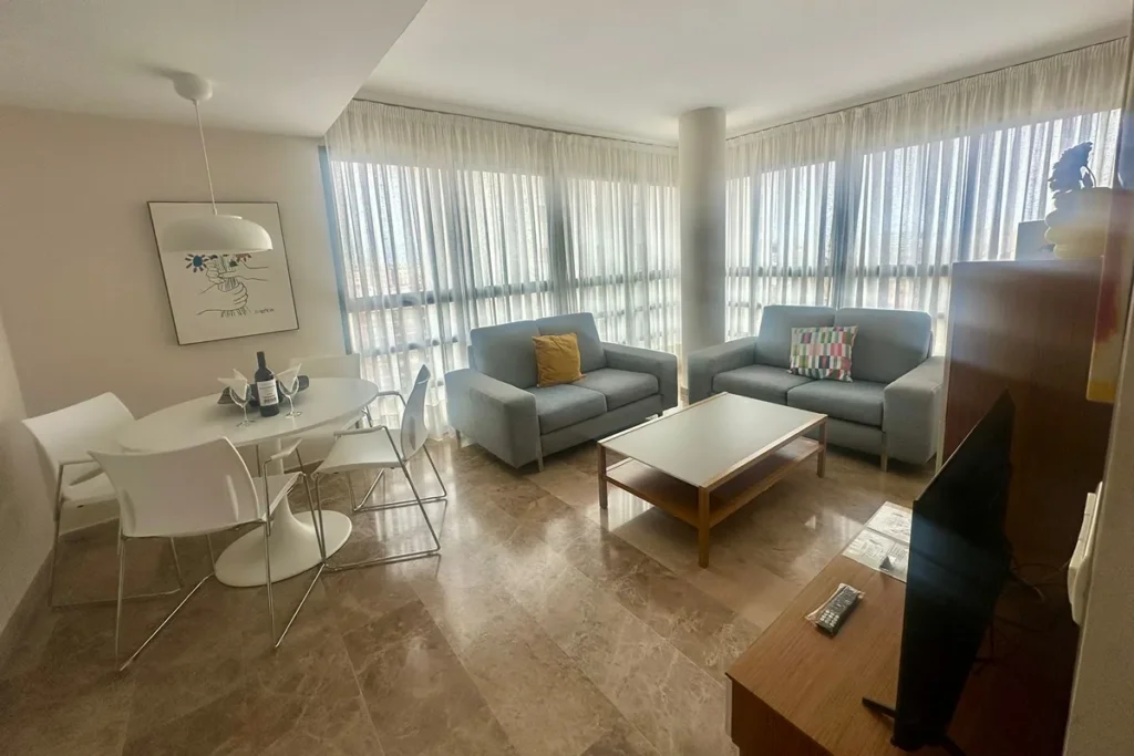 Sala de estar luminosa con cortinas, dos sillones y mesa de centro.