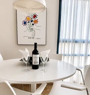 Mesa blanca con botellas y copas junto a una ventana con cortinas