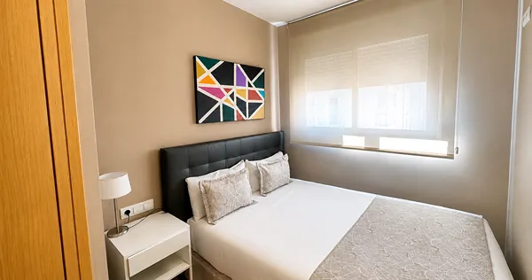 Dormitorio moderno con cama doble, l&aacute;mpara y cuadro geom&eacute;trico