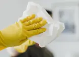 Guantes amarillos limpian un dispensador con soluci&oacute;n desinfectante