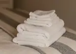 Toallas blancas dobladas apiladas sobre una cama con manta.