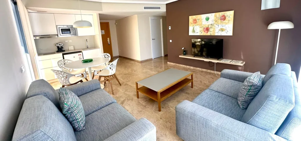Sala de estar con sof&aacute; gris, mesa baja y cocina abierta con microondas