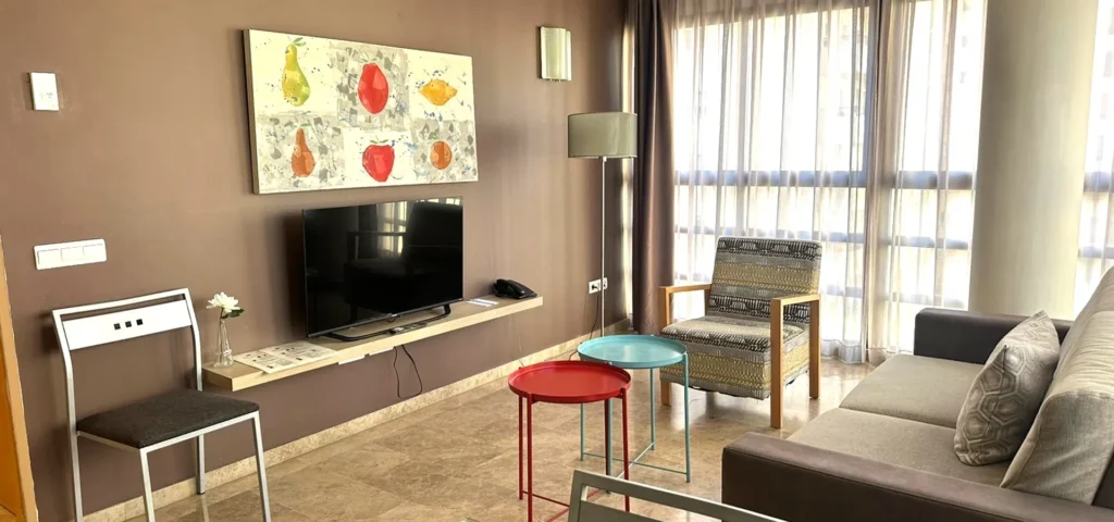 Sala de estar moderna con TV, cortinas y mesa roja y azul.