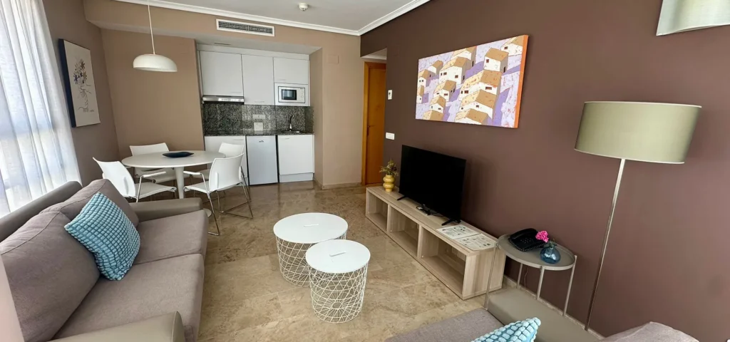 Sala de estar moderna con sof&aacute;, TV, cocina integrada y mesa de centro blanca