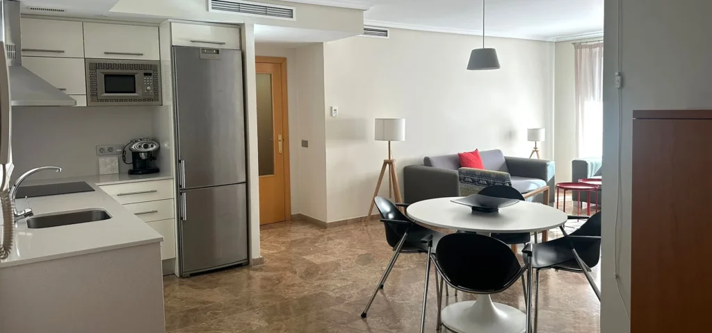 Cocina y comedor moderno con mesa redonda y sof&aacute;s grises, luz natural