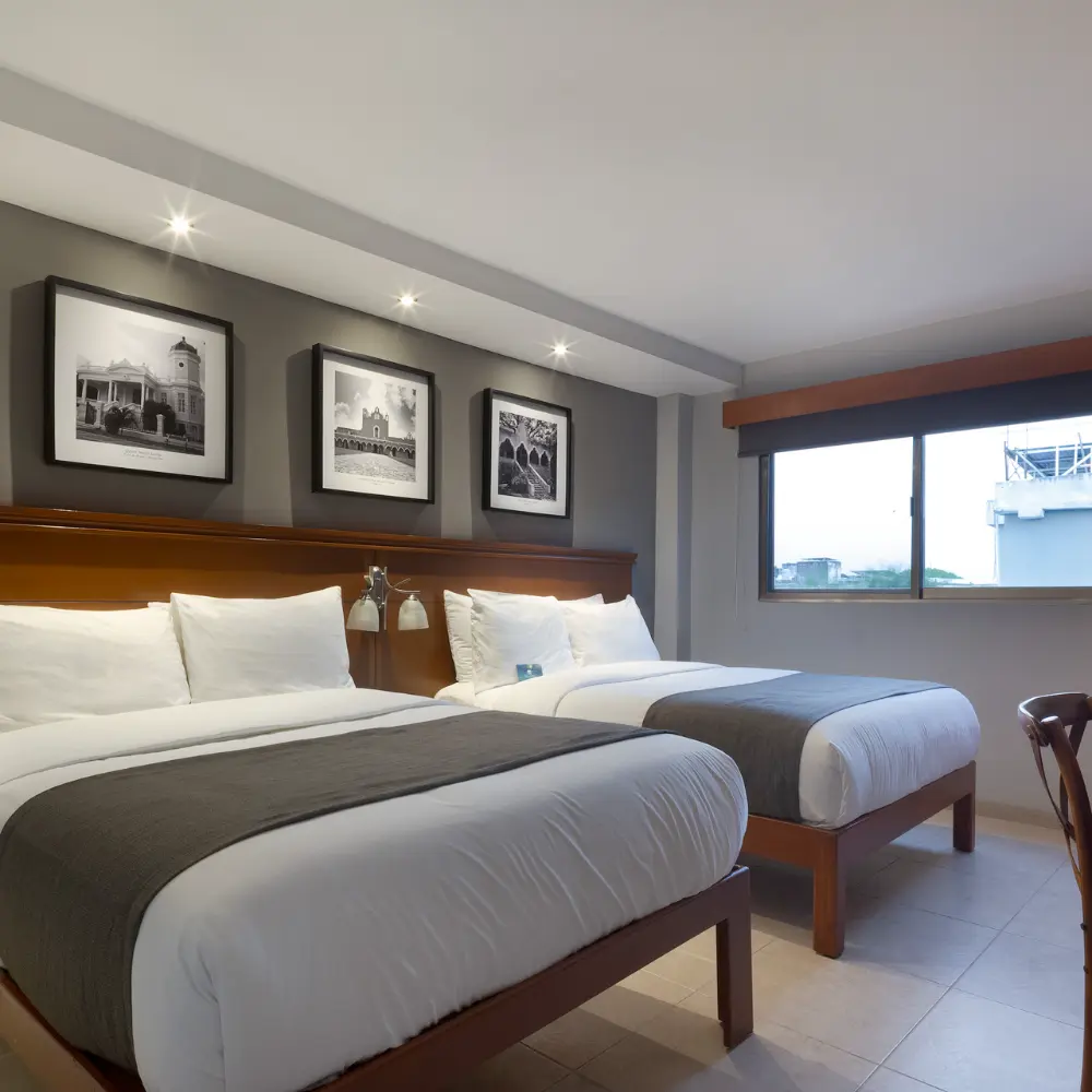 Habitaci&oacute;n de hotel con dos camas, cojines blancos y luz LED en el techo