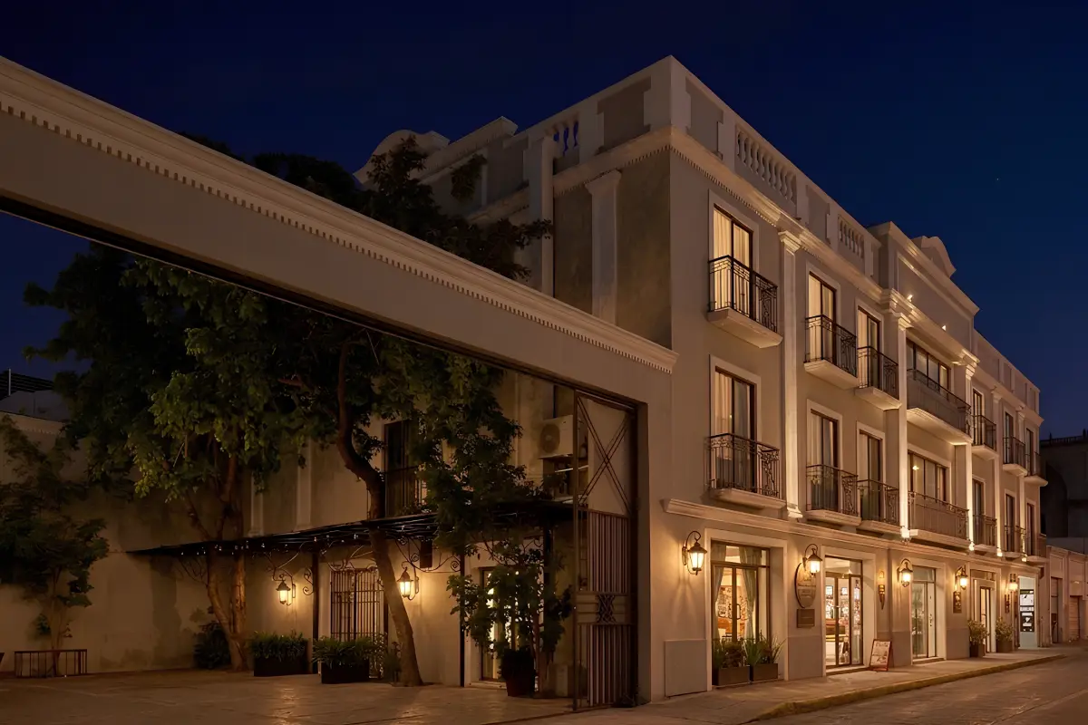 Hotel de estilo cl&aacute;sico iluminado de noche, con balcones y fachada blanca