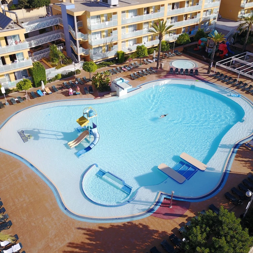 Piscina al aire libre con tumbonas y edificio hotelero, vista desde arriba