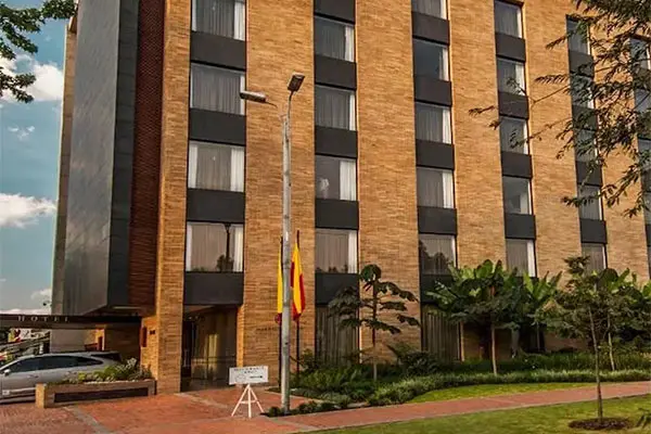 Edificio de ladrillo y ventanas con banderas y jardines frente.