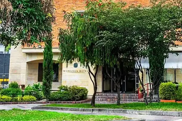 Entrada de edificio con &aacute;rboles y jard&iacute;n, fachada de ladrillo y letrero.