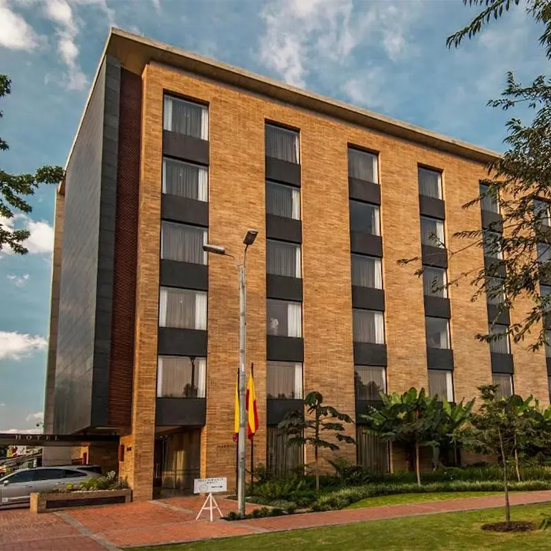 Edificio de ladrillo con banderas, jard&iacute;n y entrada bajo un cielo nublado