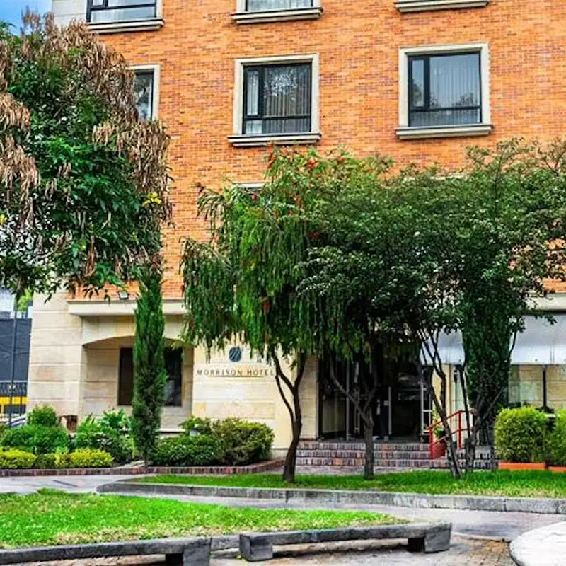 Fachada de ladrillo con ventanas y jard&iacute;n verde frente a un hotel.