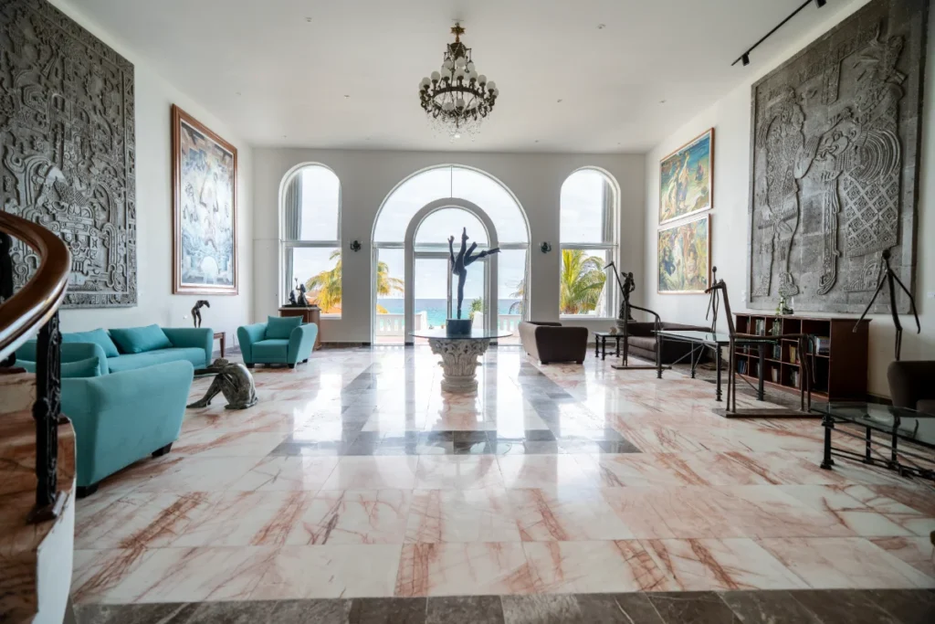 Sala amplia con sof&aacute;s turquesa, estatuas y arcos con vista al mar.