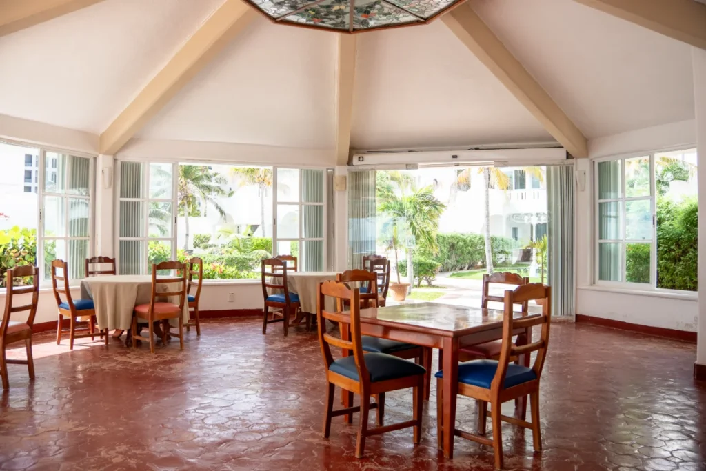 Comedor luminoso con mesas y sillas de madera, vista al jard&iacute;n tropical