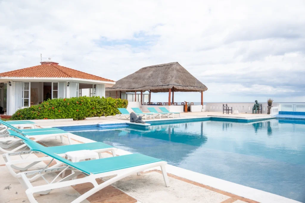 Piscina con tumbonas y caba&ntilde;a con techo de paja frente al mar