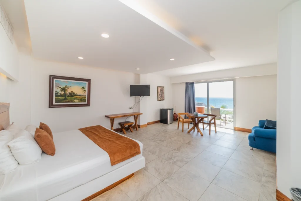 Sala blanca con sof&aacute;, mesa, TV y vista al mar por la ventana.