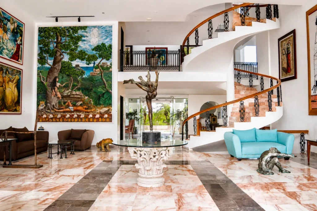 Lobby con escalera curva, sof&aacute; azul y mural de arte en una sala amplia