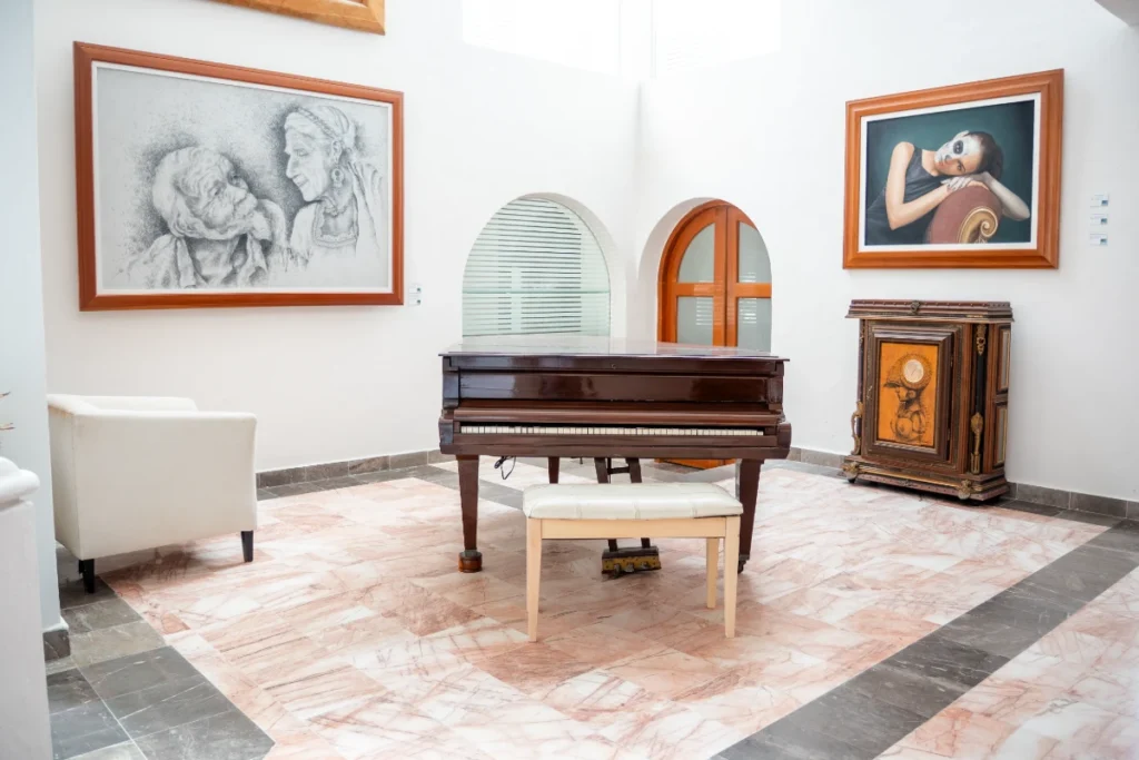 Sala de museo con piano, bancos y cuadros, vitrina antigua y suelo marmolado