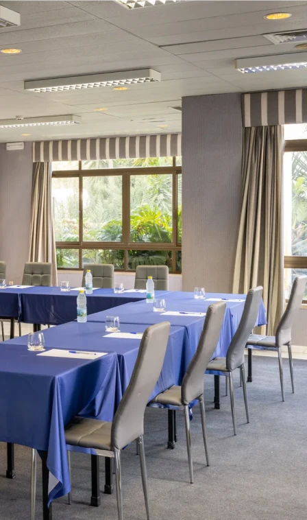 Sala com mesa de reuni&atilde;o azul e cadeiras com janelas ao fundo
