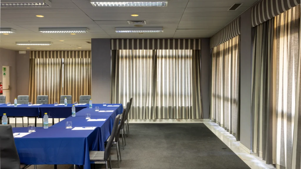 Sala de reuni&atilde;o com mesas cobertas e cortinas listradas bege e marrom