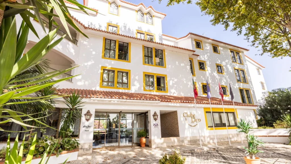 Fachada de hotel branco com janelas amarelas, varandas e bandeiras.