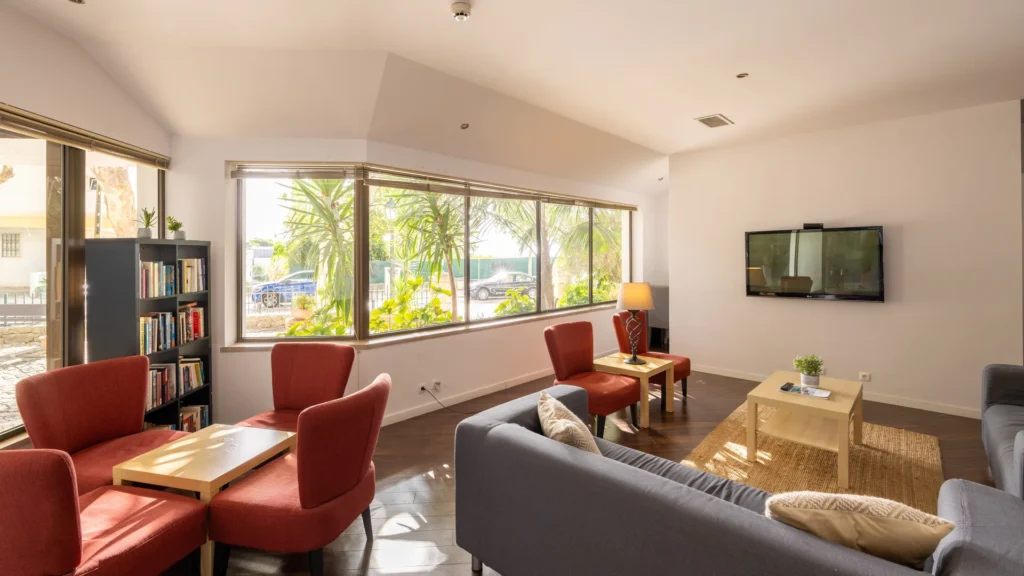 Sala de estar moderna com sof&aacute;, poltronas e grandes janelas com vista verde