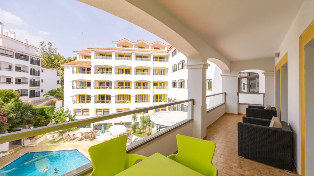 Varanda com vista para piscina e hotel branco com janelas amarelas