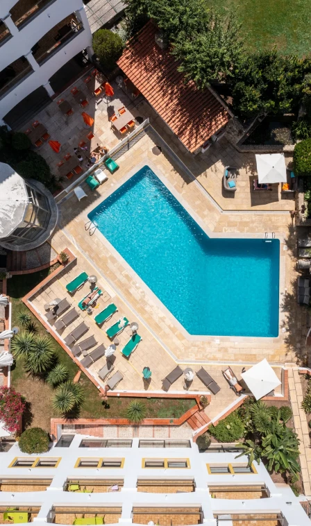 Vista a&eacute;rea de piscina azul, espregui&ccedil;adeiras e &aacute;rea externa de hotel.