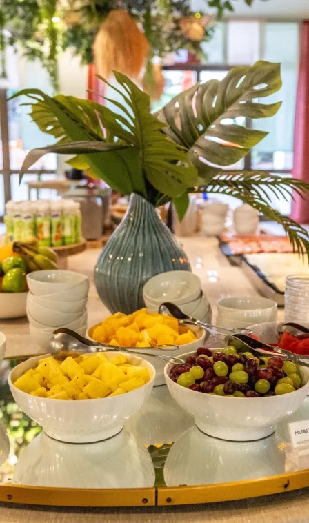 Mesa de caf&eacute; da manh&atilde; com frutas em tigelas e folhagens tropicais ao fundo