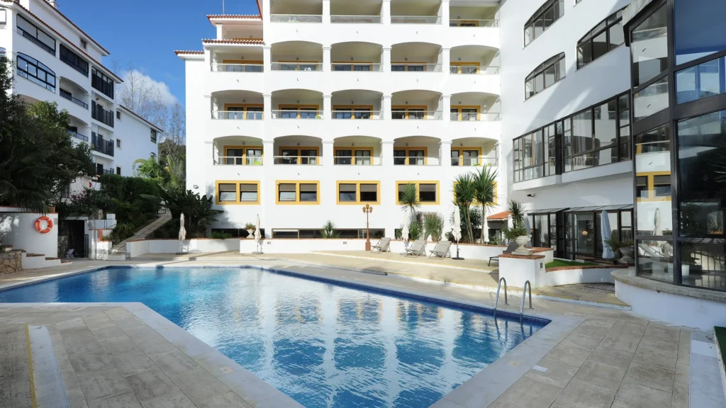 Piscina azul em frente a hotel moderno com varandas brancas e guarda-s&oacute;is