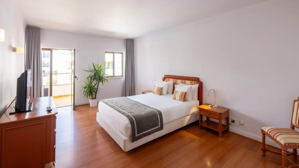 Quarto de hotel com cama, mesa de cabeceira, poltronas e janela ampla