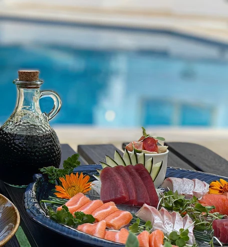 Prato com sushis e sashimi, garrafa decorativa e piscina ao fundo