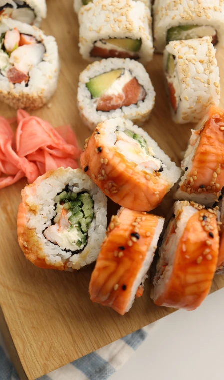 Fatias de sushi com salm&atilde;o, pepino e cebolinha, sobre t&aacute;bua de madeira