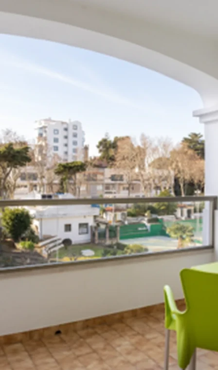 Vista de jardim e edif&iacute;cios ao fundo a partir de varanda com cadeira verde
