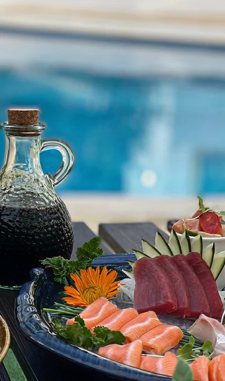 Jarra com peixe fatiado e salada, ao lado de uma piscina ao fundo.