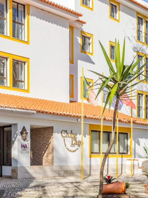 Fachada do Clube d&rsquo;Azeite com bandeiras, palmeira e janelas amarelas.