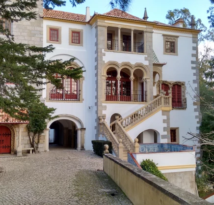 Fachada de casa colonial com escadaria, janelas e arcos, em p&aacute;tio de pedra.