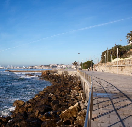 Vista do litoral com mar, pedras e cal&ccedil;ad&atilde;o sob c&eacute;u azul