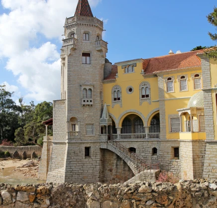 Pal&aacute;cio hist&oacute;rico amarelo e branco com torre e arcos sobre pedra.