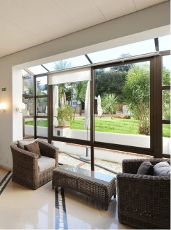 Sala com sof&aacute; e vista para jardim atrav&eacute;s de grandes janelas de vidro