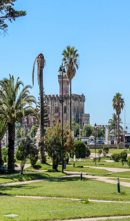 Castelo medieval com torres ao fundo e jardim com palmeiras em dia ensolarado