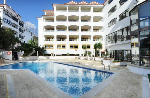 Piscina ao ar livre em hotel branco com varandas e jardim ao lado