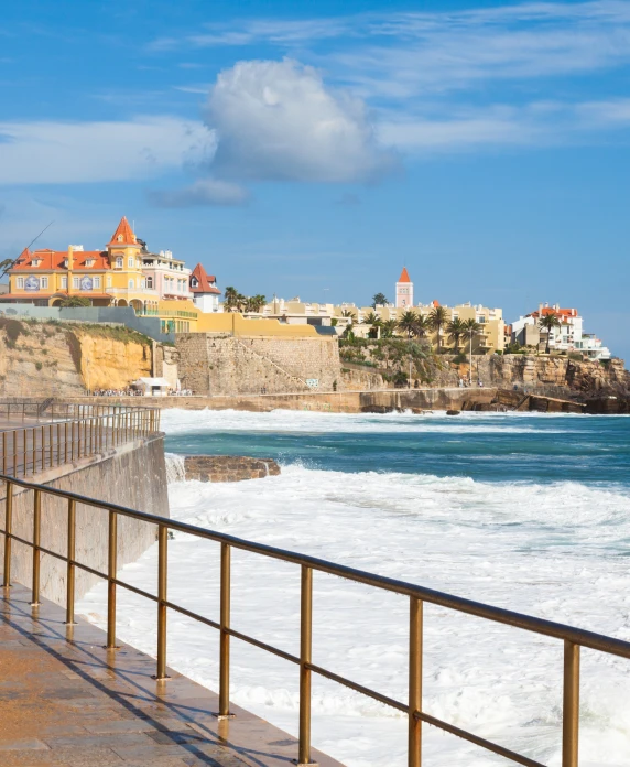Vista costeira com ondas e edif&iacute;cios coloridos sobre penhasco ao c&eacute;u azul